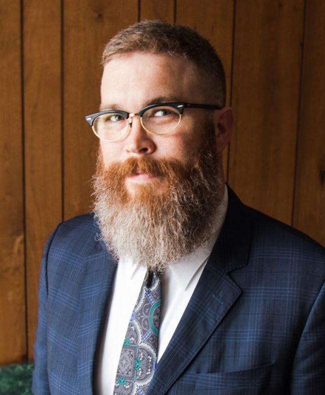 Portrait of Mike Wright wearing a blue suit and tie and glasses.