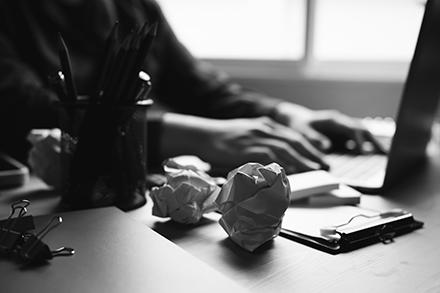 A person's hands at a computer with two crumpled balls of paper to the side.
