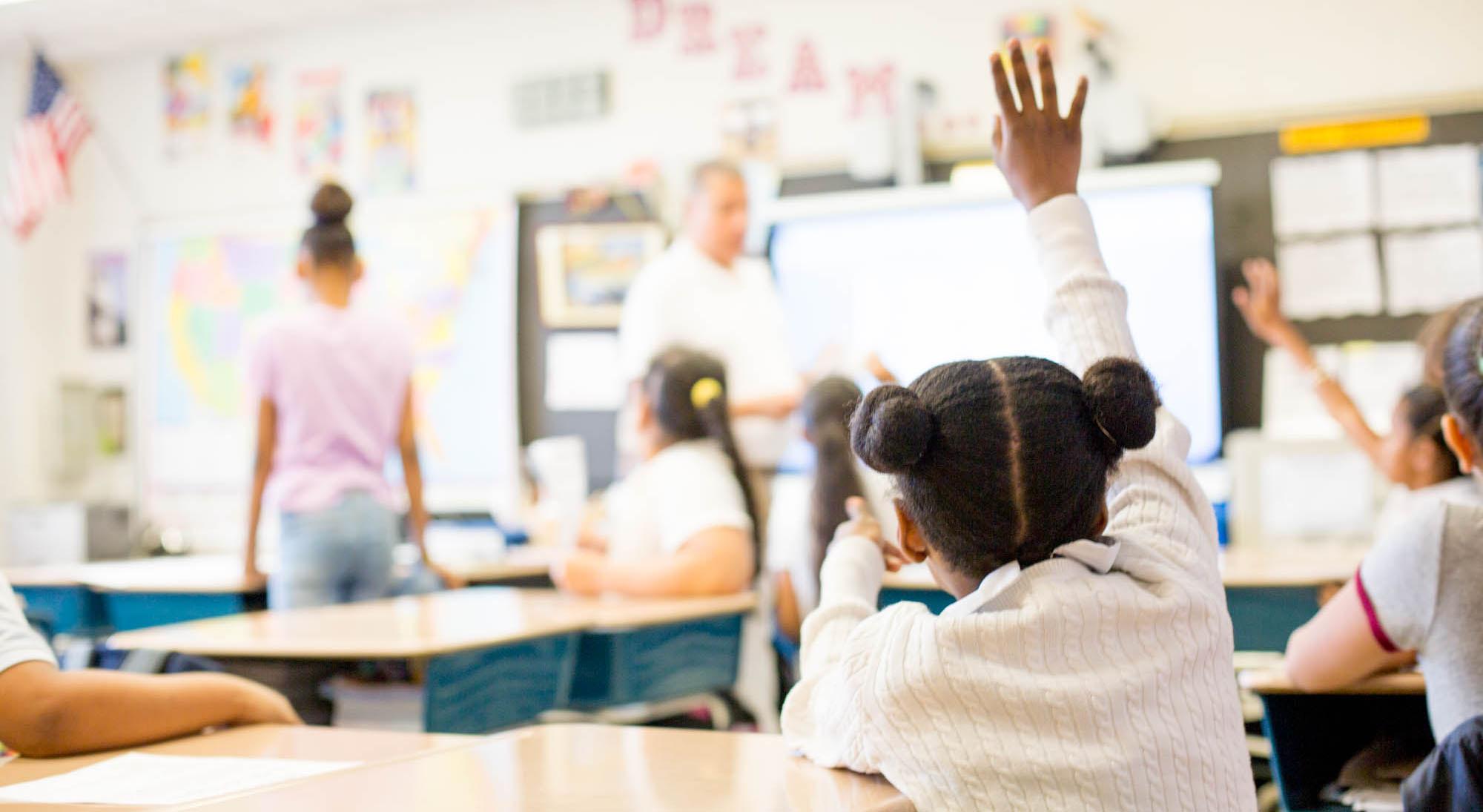 A young girl raising her hand in a classroom.