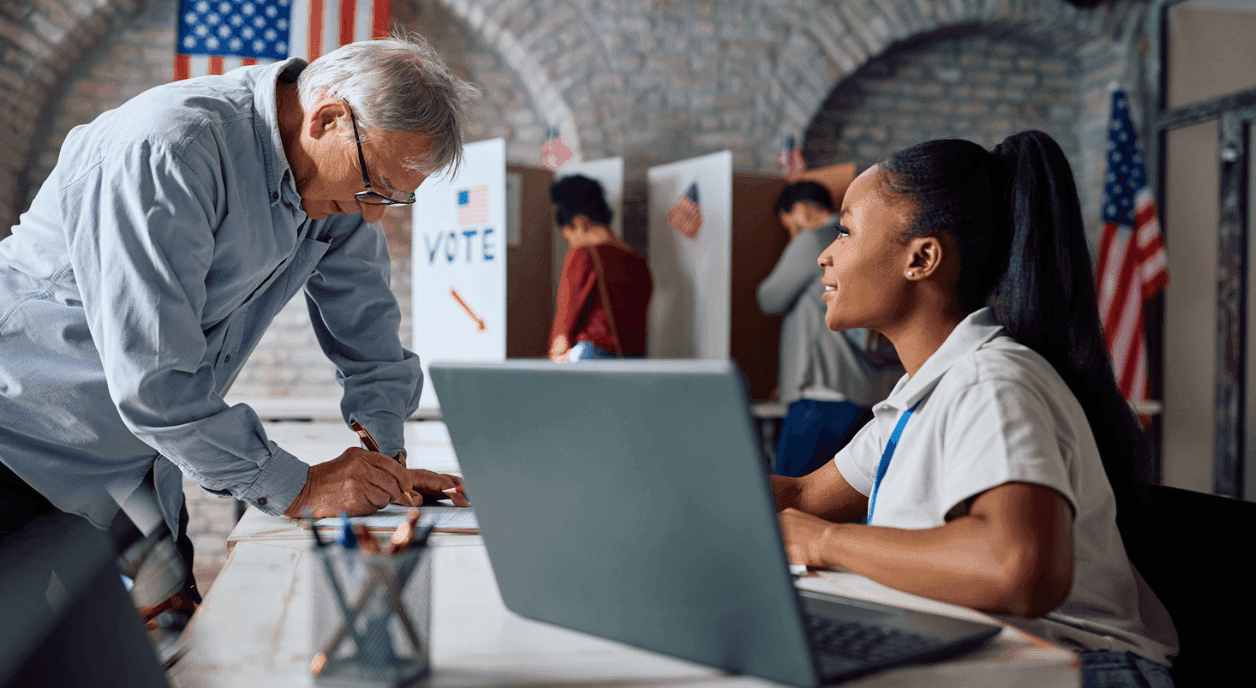 A woman helping an older man vote at the polls.