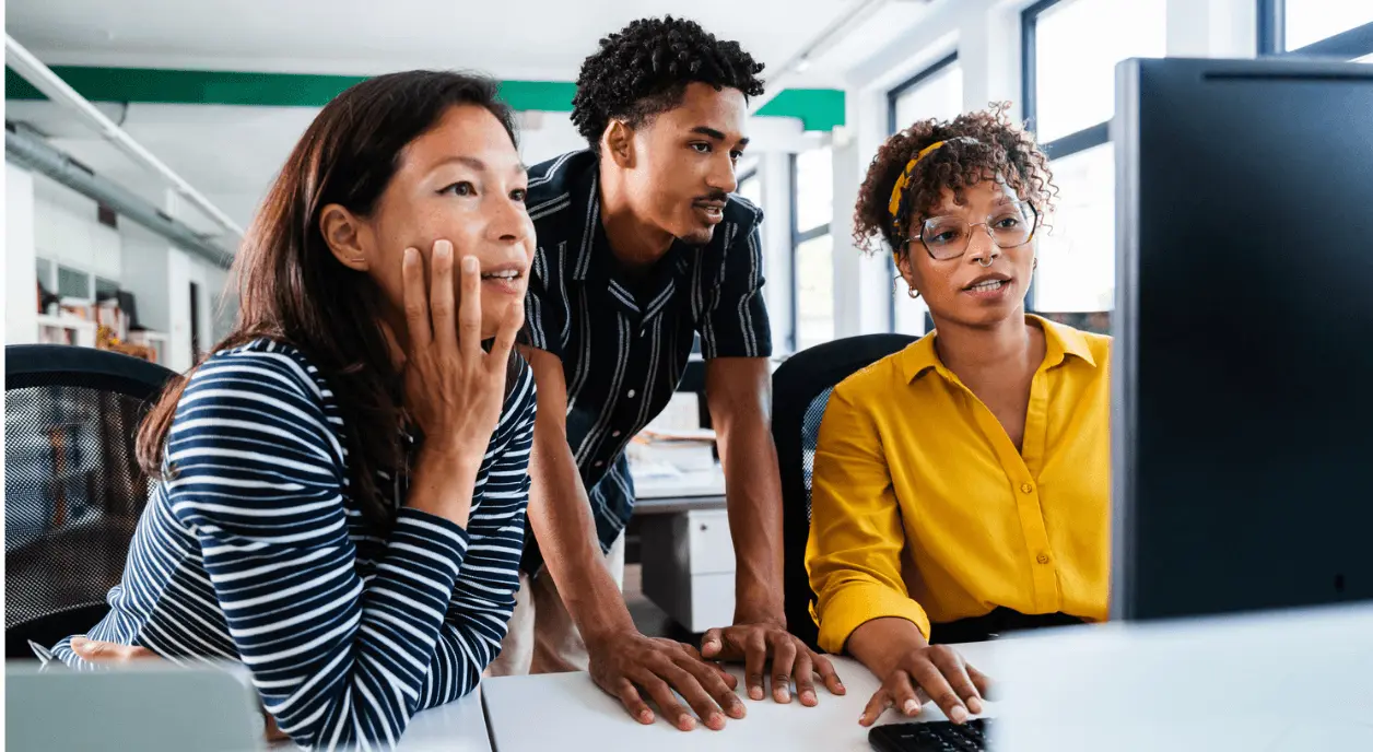 Three staff members looking hopefully at a computer screen in an office.