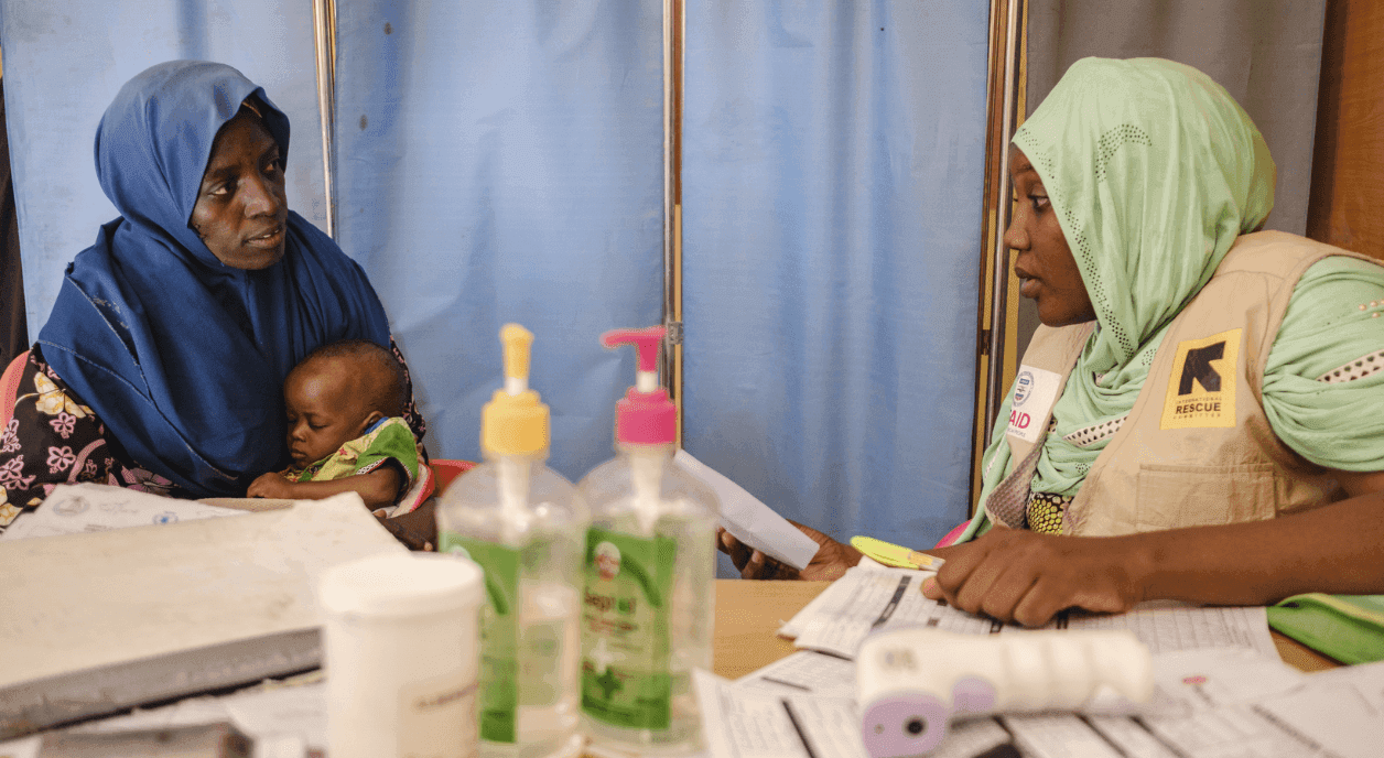 A women working for an international aid group helps a mother and child.